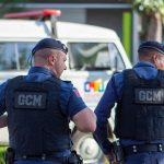 Dois guardas municipais uniformizados patrulham uma rua.