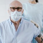 Profissional de saúde aplica uma vacina no braço de um homem idoso em ambiente clínico.