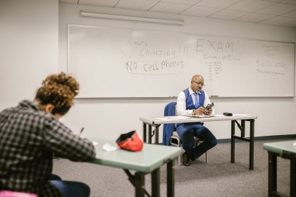 Fiscal acompanha estudantes durante a realização de uma prova em uma sala de aula.