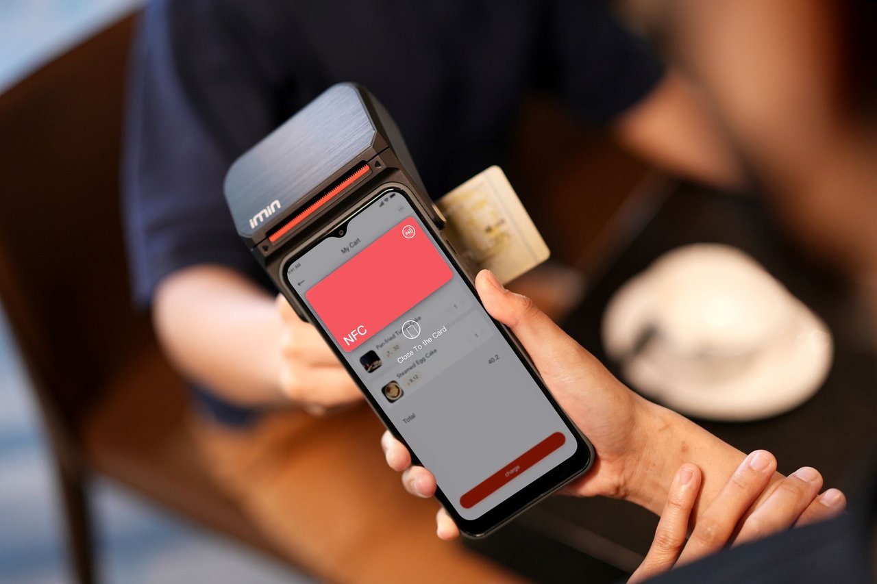 Close de uma mão aproximando um smartphone de um terminal para realizar um pagamento por NFC.
