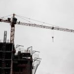 Edifício de grande porte em construção, com guindaste de torre diante de céu nublado.