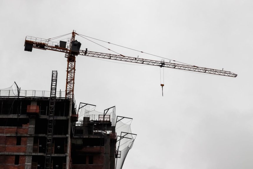 Edifício de grande porte em construção, com guindaste de torre diante de céu nublado.